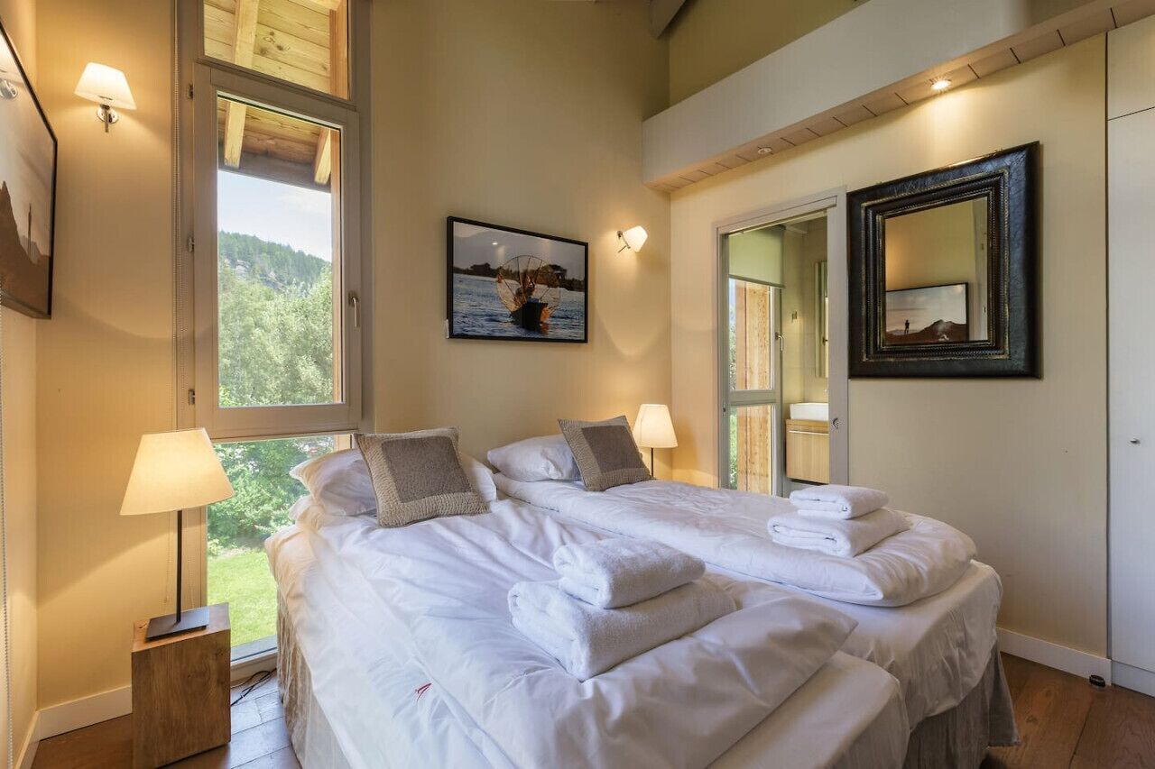 A bedroom with two beds, a large window, a painting, and a mirror.