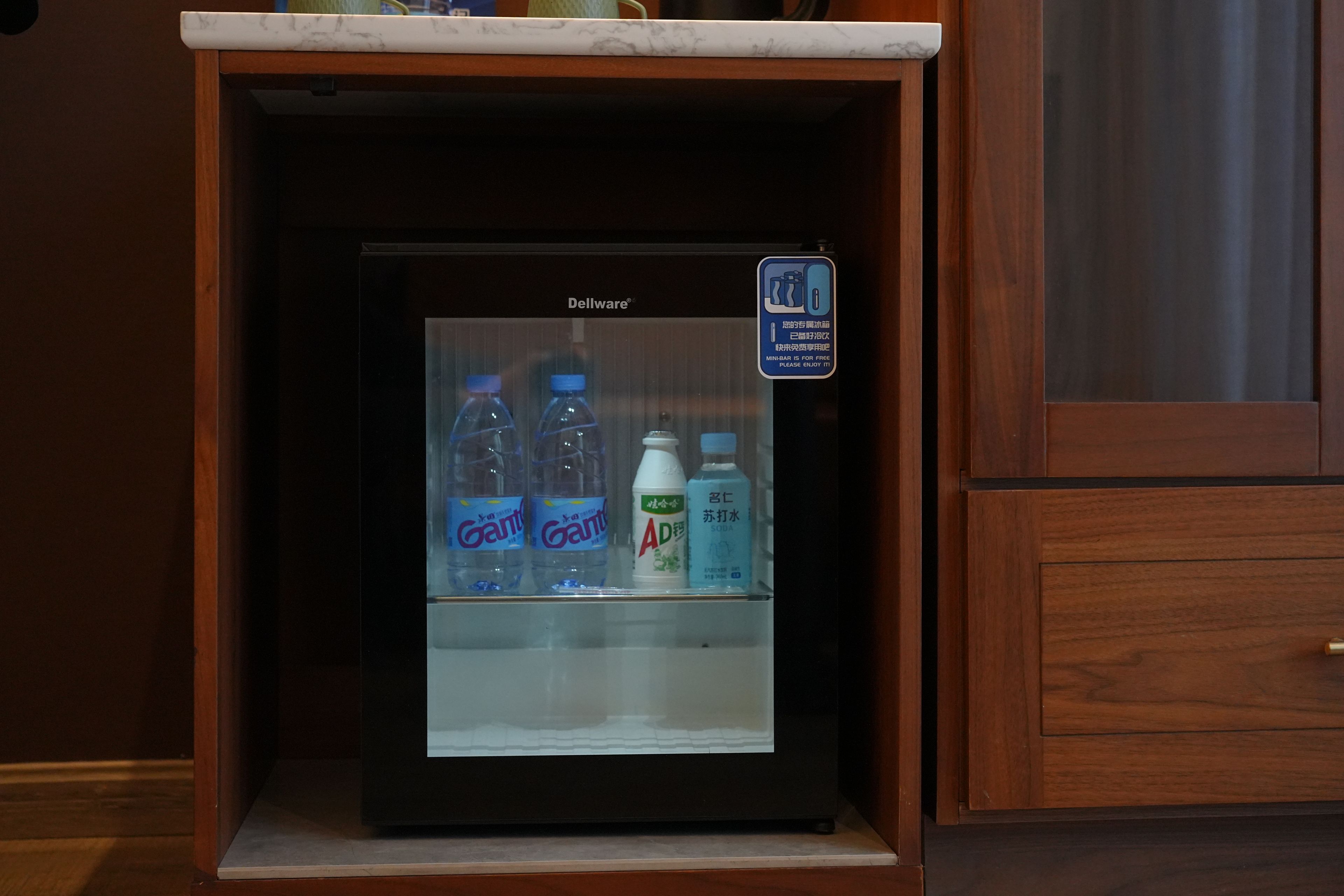 A mini-bar refrigerator with a sign indicating it is free, containing bottled water and a bottle of soda.