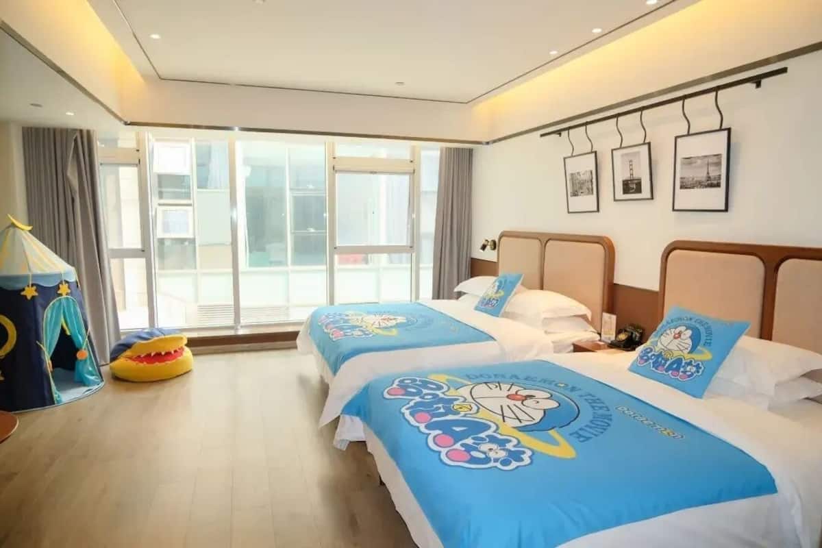 Habitación de hotel con dos camas, una tienda de juegos y un ventanal grande con cortinas.