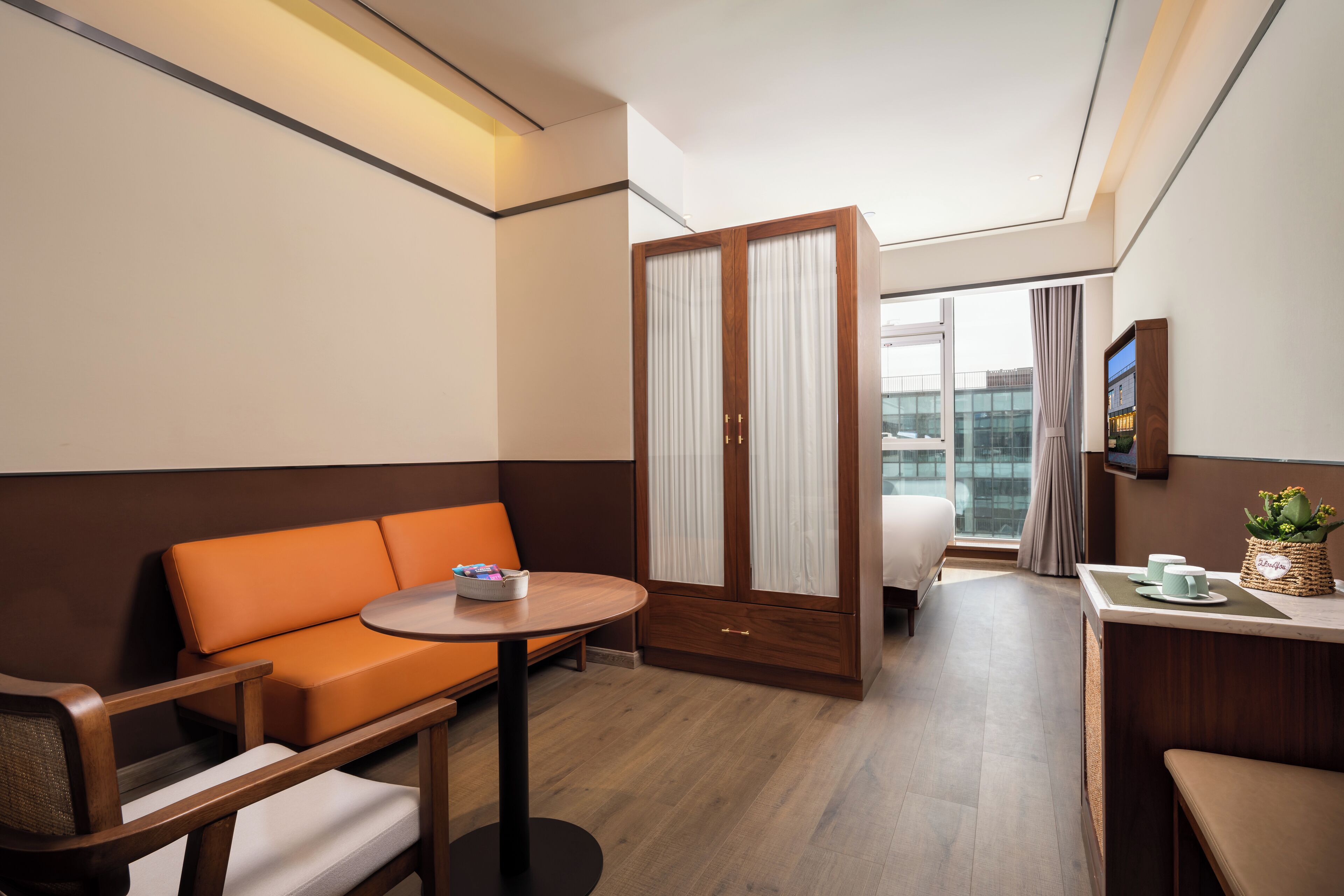 A hotel room with a sofa, a small table, a bed, and a window with curtains.