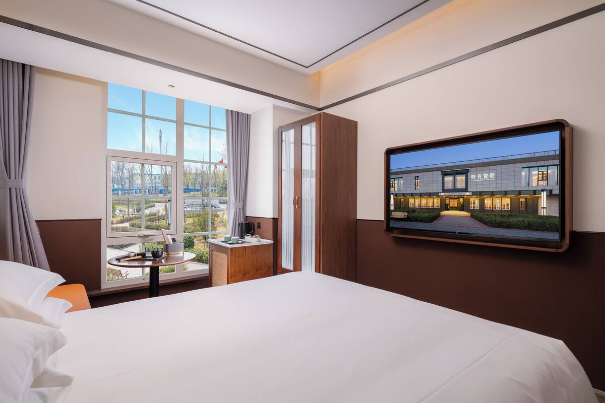 Habitación de hotel con una cama grande, un escritorio con lámpara, un televisor en la pared y una ventana con vistas al exterior.