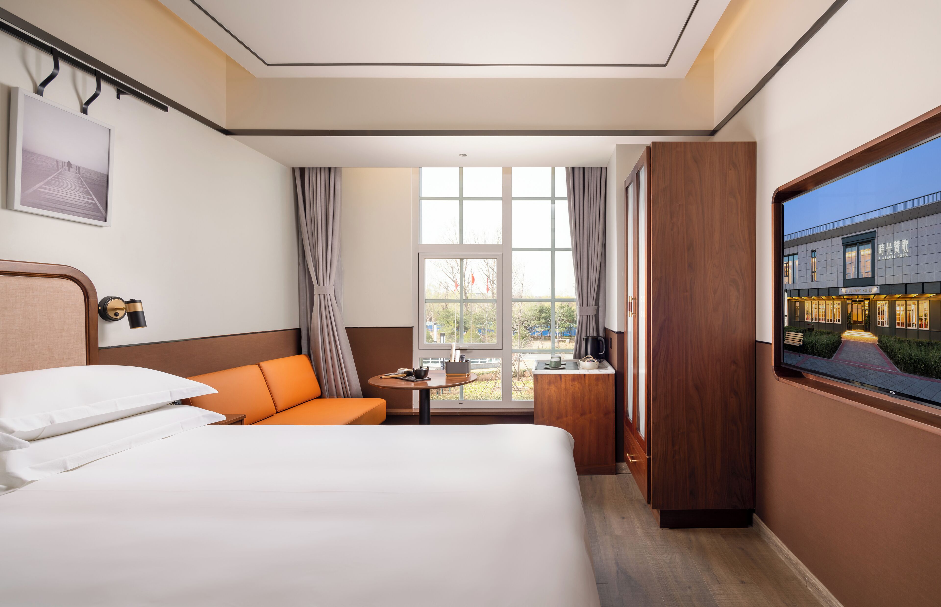 Una habitación de hotel con una cama grande, un sofá naranja, una mesita y una ventana con cortinas.
