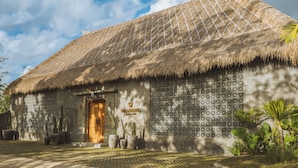 Une maison traditionnelle à toit de chaume, avec une porte en bois et des plantes en pot devant l’entrée.