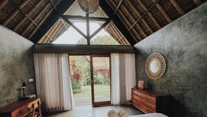 Une chambre avec un grand lit, un bureau en bois, une commode et une vue sur le jardin grâce à une porte vitrée.