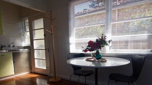 A kitchen with a wooden floor, a dining table with two chairs, and a window with blinds. - Restored one bedroom holiday flat. (Katoomba)
