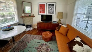 A living room with a sofa, a TV, a fireplace, and a dining table. - Restored one bedroom holiday flat. (Katoomba)