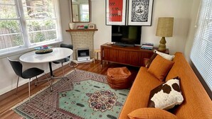 A living room with a sofa, a TV, a fireplace, a dining table, and a patterned rug. - Restored one bedroom holiday flat. (Katoomba)