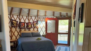 Ein Schlafzimmer mit einem Bett, Holzboden, Teppich mit Muster, einer Wand mit Kunstwerken und einer zur Außenwelt führenden Tür.