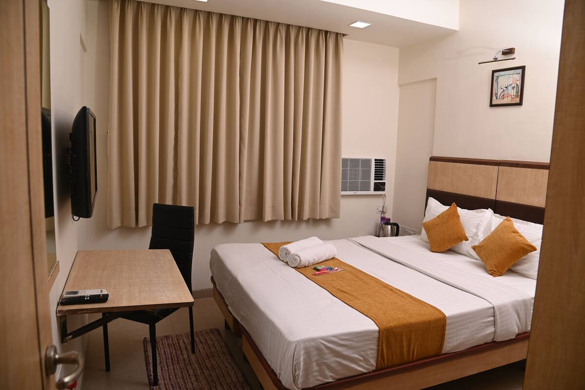 A hotel room with a bed, a desk, a chair, a TV, and a window with curtains.