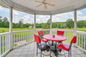 Une terrasse couverte avec une table ronde et quatre chaises rouges, donnant sur un paysage verdoyant.