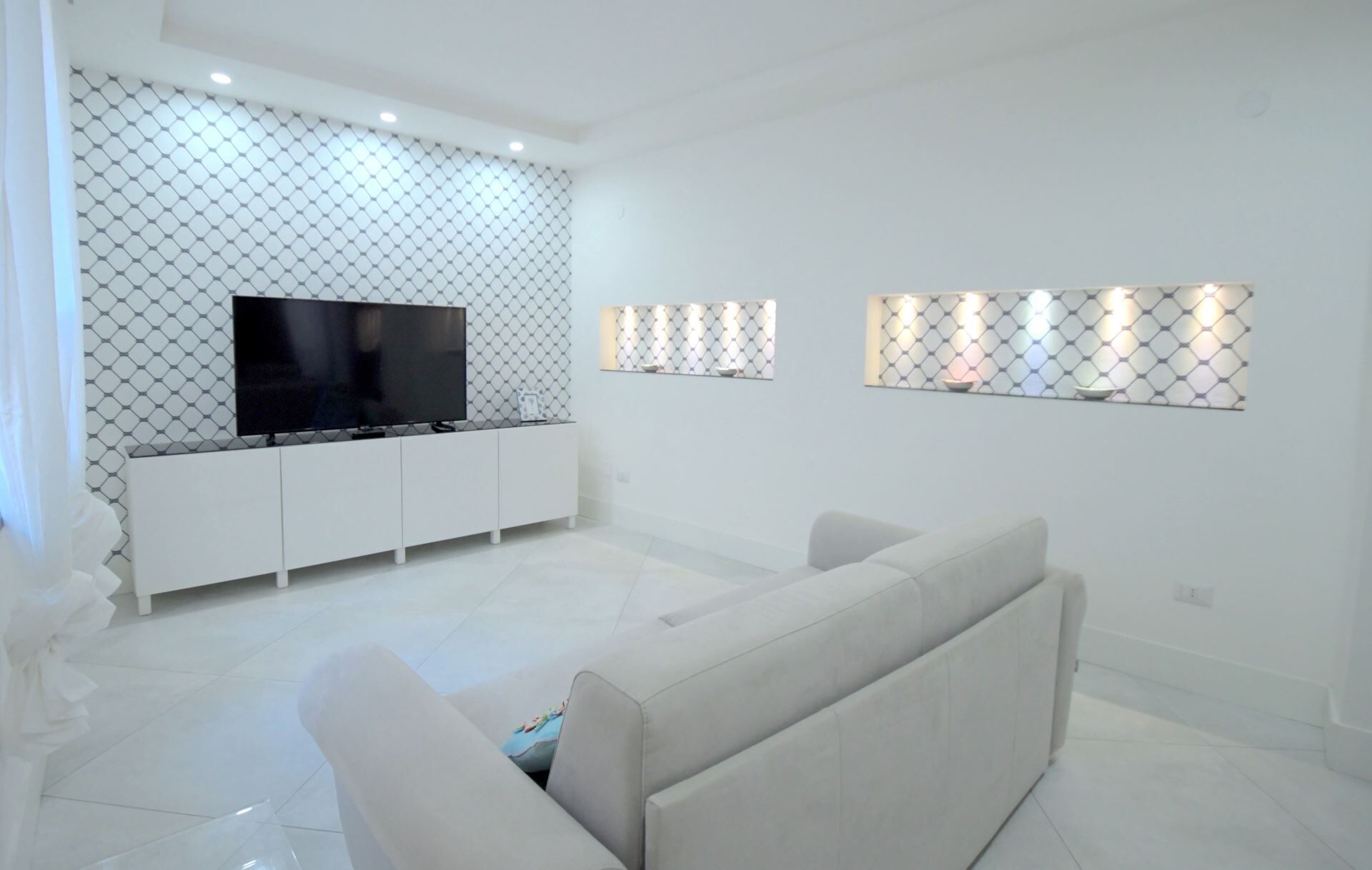A modern living room with a flat-screen TV on a white cabinet, a beige sofa, and decorative wall lights.