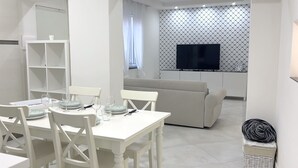 Ein modernes, minimalistisches Wohnzimmer mit Essbereich. Es beinhaltet ein Sofa, einen Fernseher und einen Esstisch mit Stühlen.