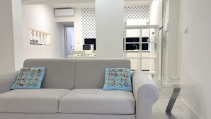 Ein modernes Wohnzimmer mit einer Couch und Zierkissen, im Hintergrund eine Küche und eine Treppe, die zu einer anderen Ebene führt.