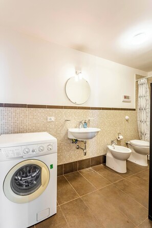 Een kleine badkamer met een wasmachine, wastafel en twee toiletten.
