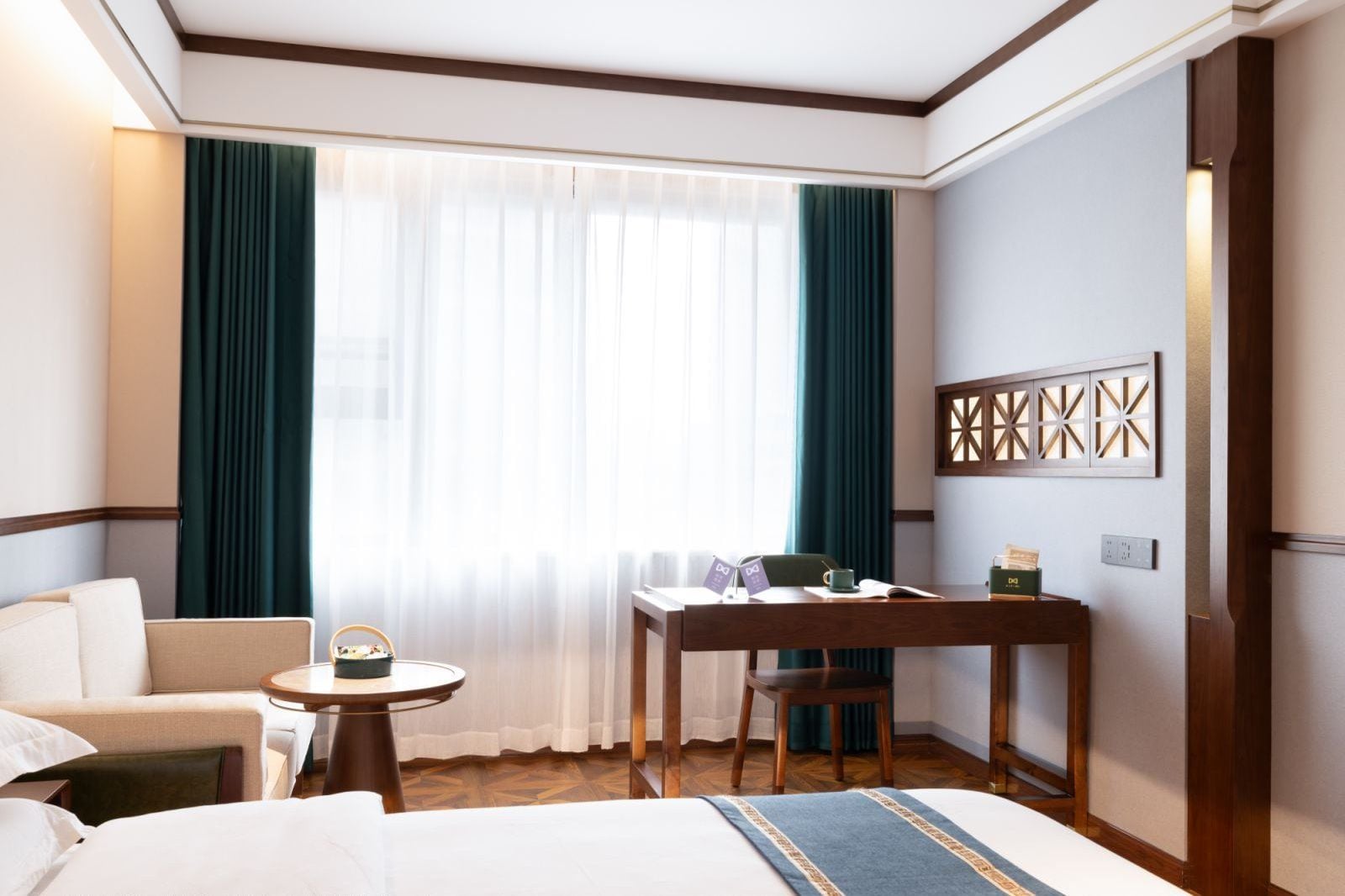 Ein Hotelzimmer mit Bett, Schreibtisch, Stuhl, kleinem Tisch und einem Fenster mit Vorhängen.