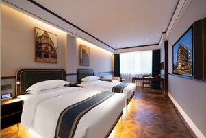 A hotel room with two beds, a desk, a chair, and a large window.