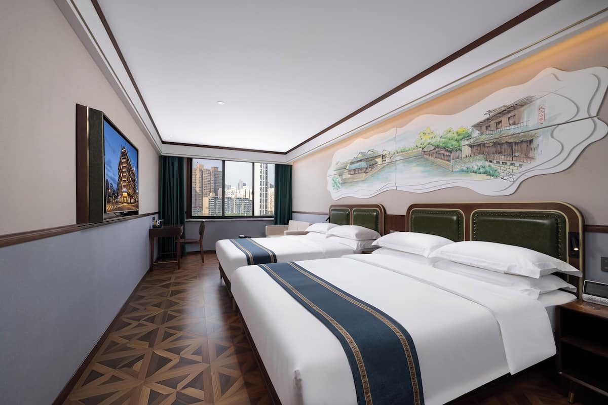 A hotel room with two beds, a city view, a painting of a traditional building, and a geometric patterned floor.