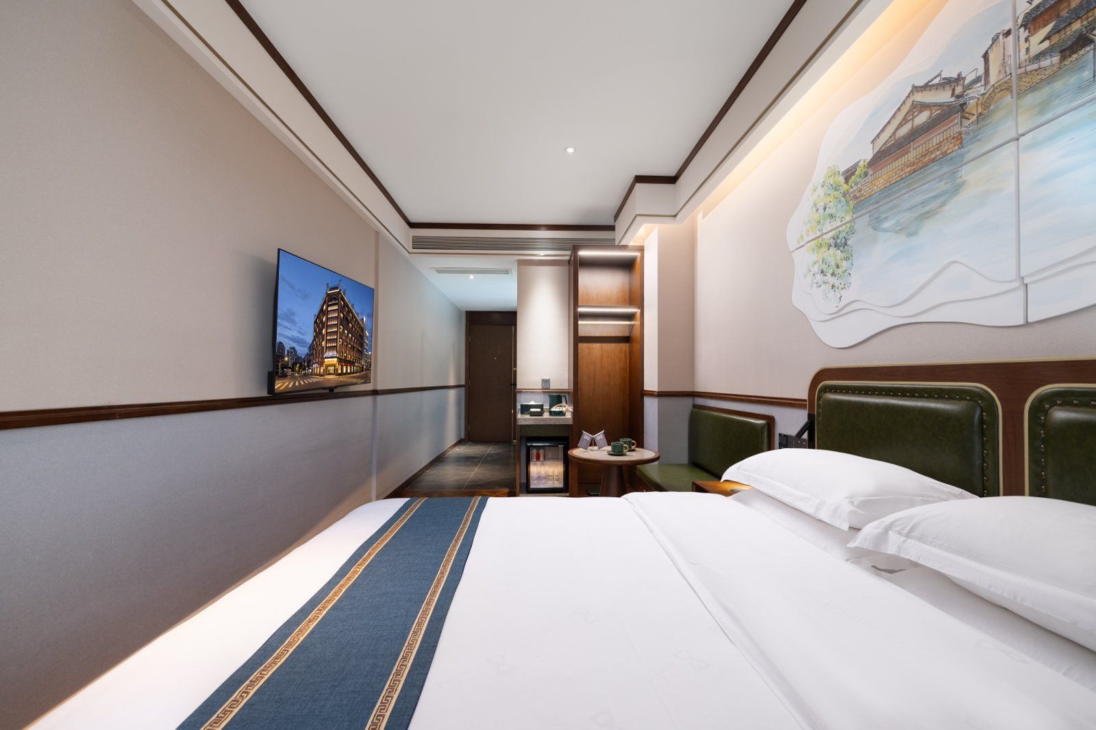 Habitació d'hotel amb un llit gran, una taula petita, una cadira, un quadre a la paret i vista d'un edifici a través de la finestra.