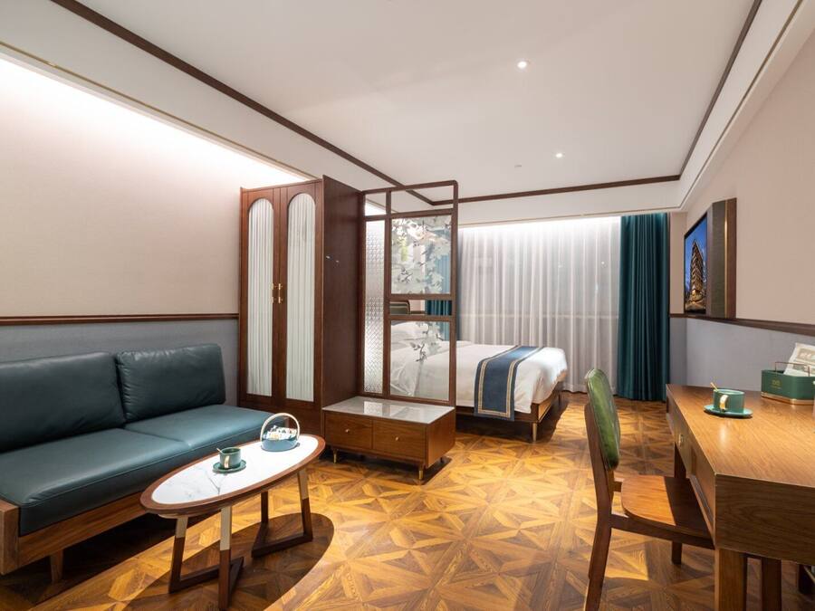 A hotel room with a sofa, a bed, a wooden desk, a small table, and a chair.