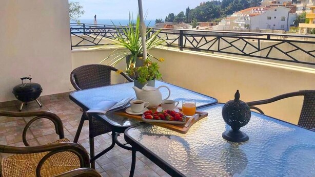 A balcony with a table set for breakfast, including a pitcher, cups, strawberries, and orange juice.