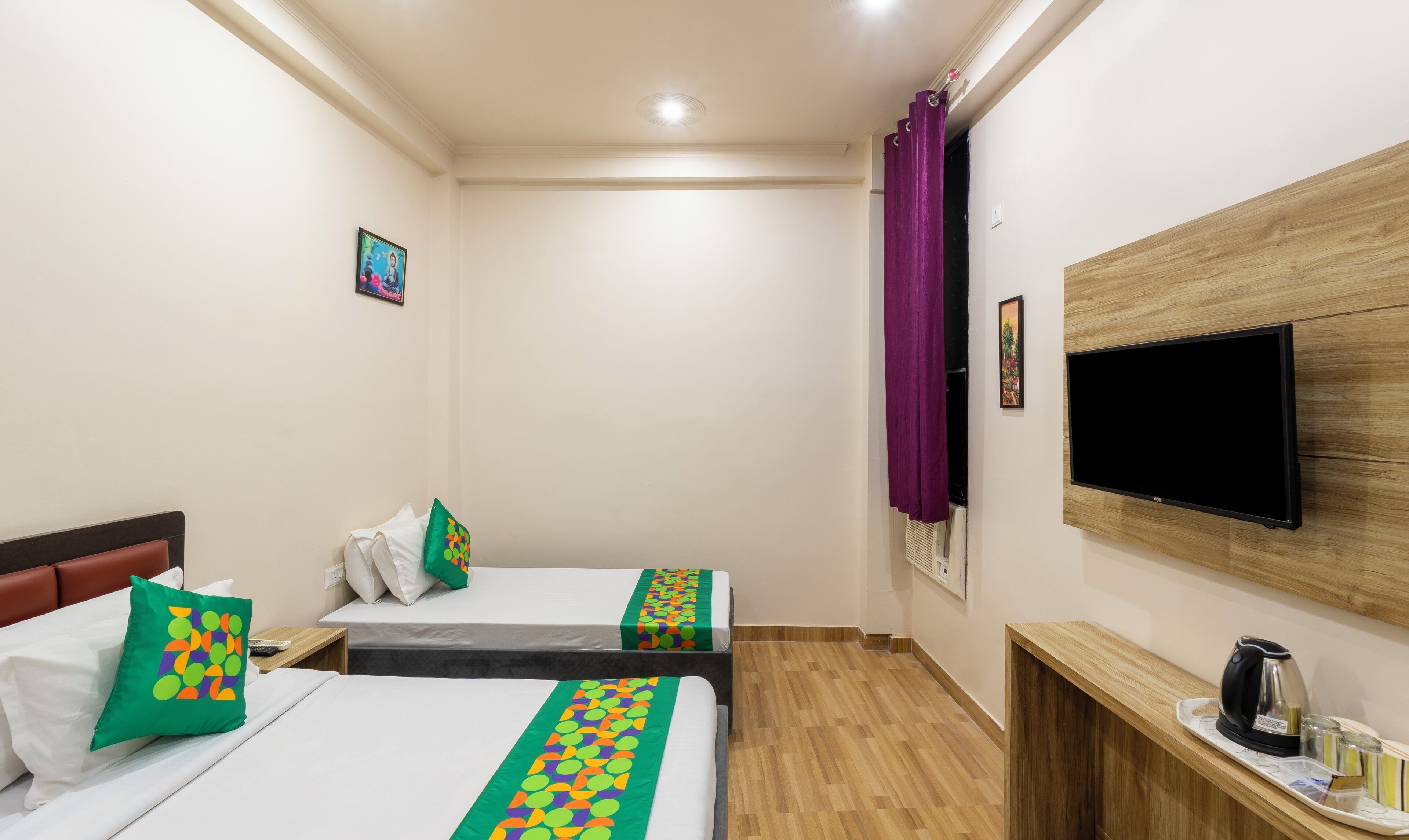 A hotel room with two beds, a TV, a wooden cabinet with a kettle, and a tray with glasses and a kettle.