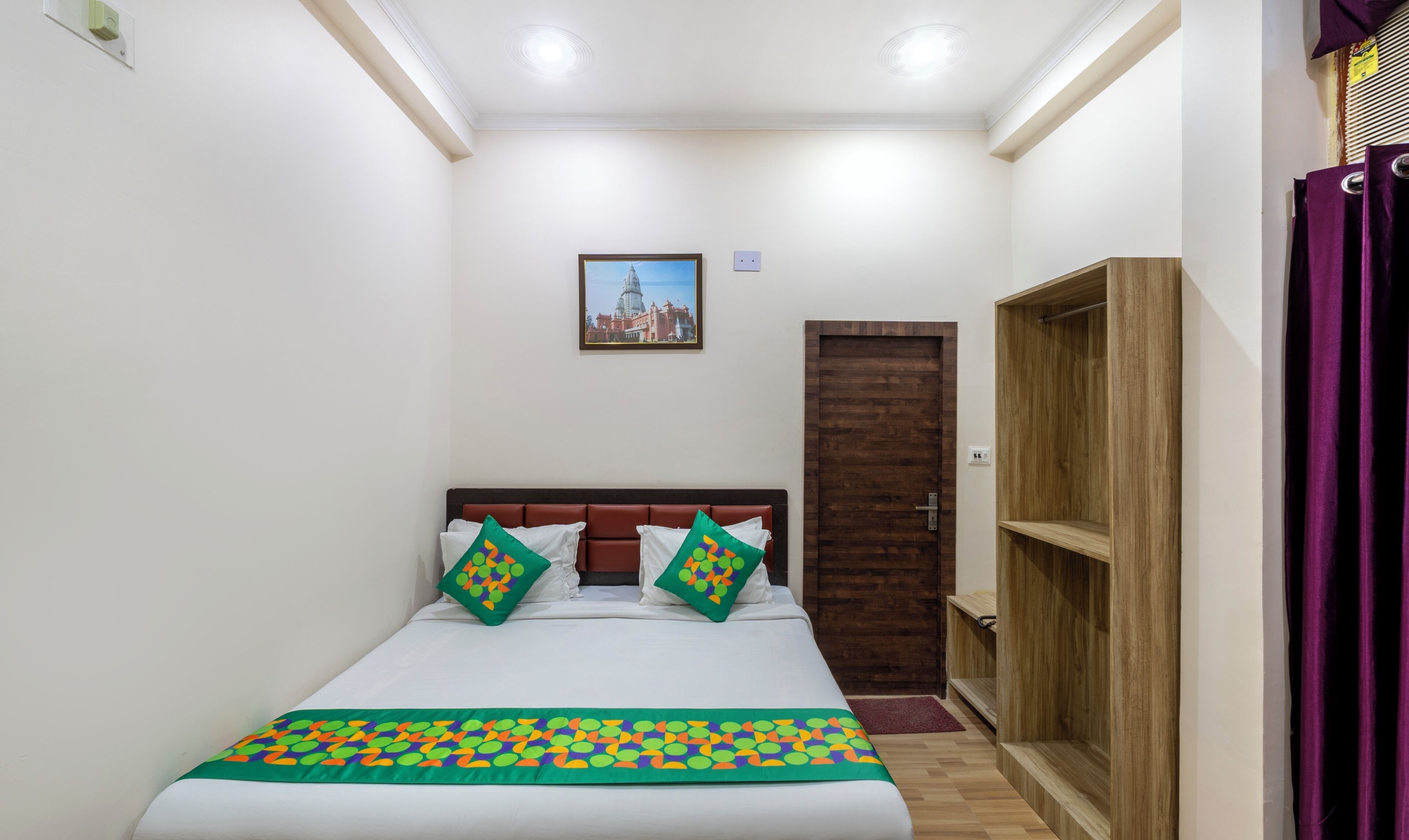 A small, well-lit bedroom with a bed, a wooden wardrobe, and a door.