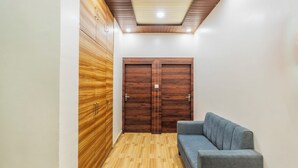 A hallway with wooden wardrobes, a grey sofa, and a wooden floor. - Treebo Om Shree Banaras (Varanasi)