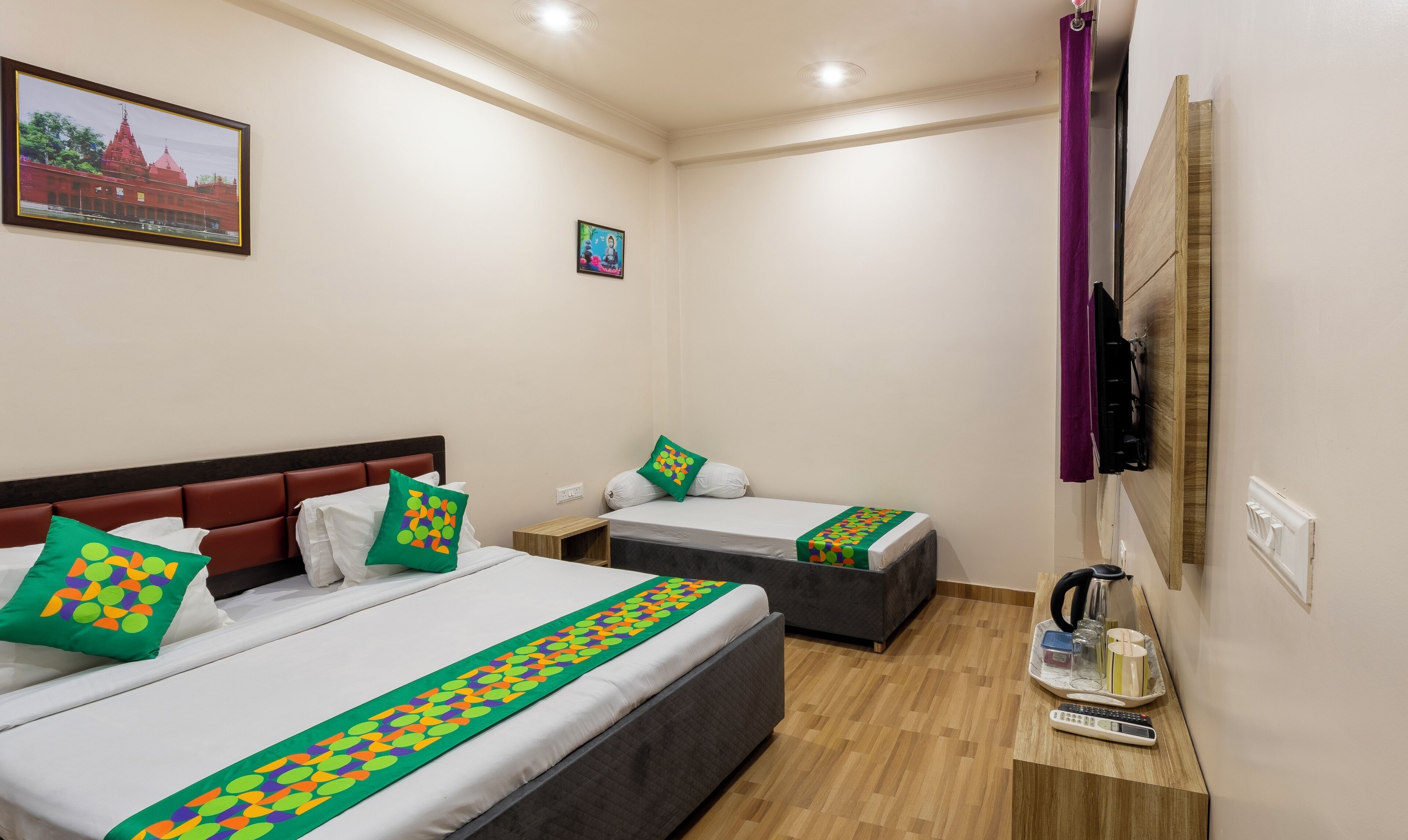 Une chambre d’hôtel avec deux lits, une table de chevet en bois, une télévision et un tableau représentant un temple accroché au mur.