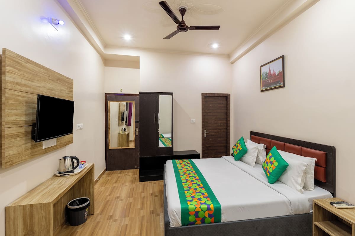A hotel room with a bed, a TV, a ceiling fan, a wooden desk, a mirror, and a door.