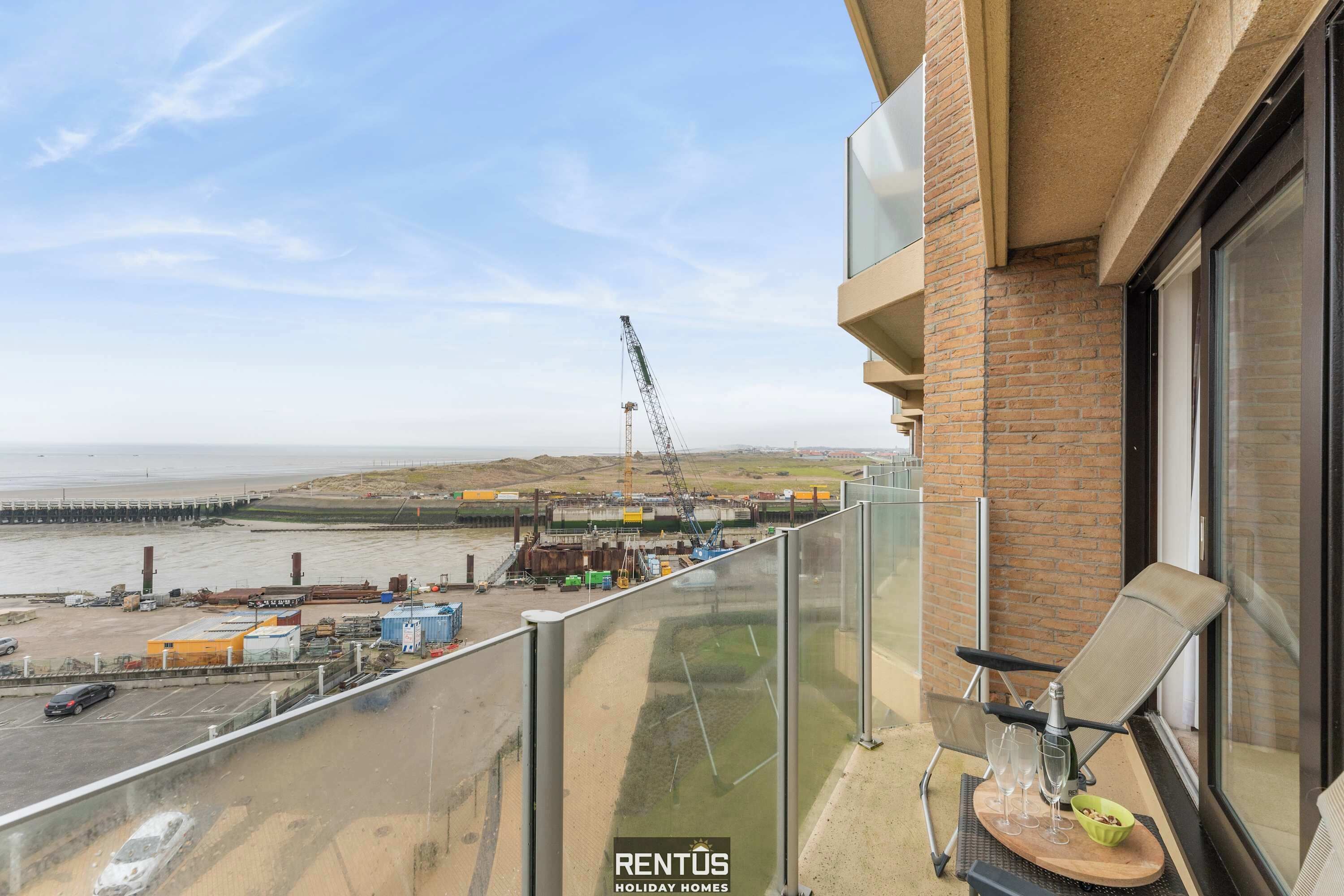 Ein Balkon mit Blick auf eine Baustelle, einen Kran und einen Strand.