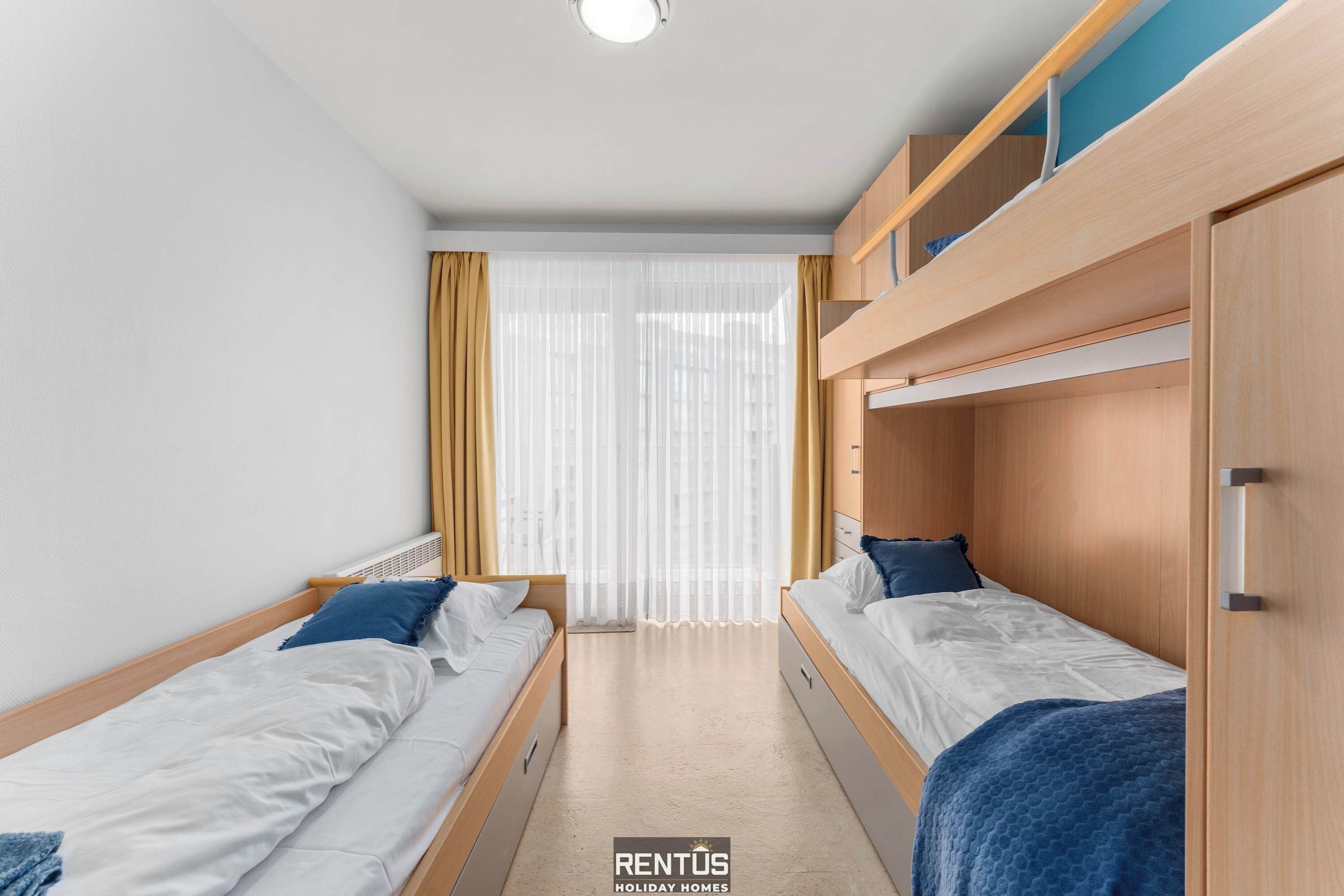 A bedroom with two single beds, a window with curtains, and a bunk bed.