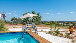 Ein Schwimmbecken mit Holzterrasse, einer Leiter und einem weißen Sonnenschirm.