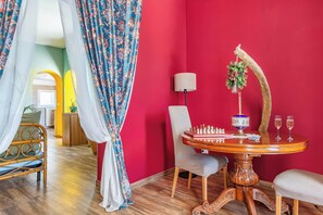 A room with a red wall, a wooden table with a chess set, two chairs, a lamp, and a hanging plant. - Gioberti 20 I Trulli With Pool (Martina Franca)