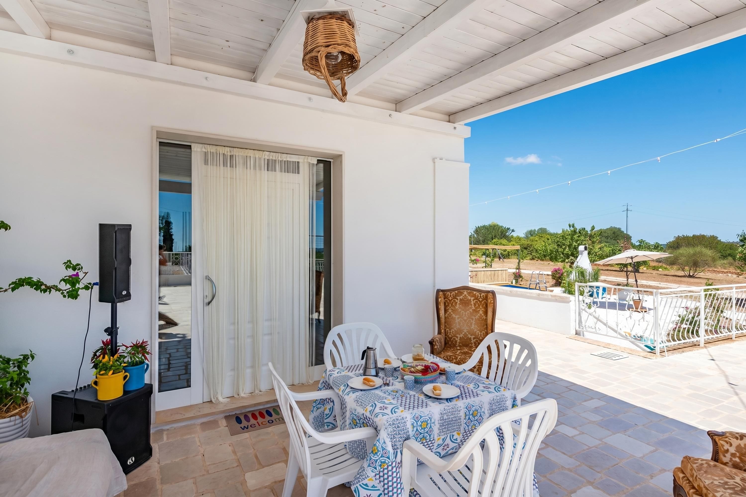 Un balcon avec une table dressée pour le dîner, des chaises blanches, une suspension en osier et une vue sur le paysage.