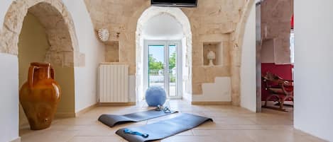 A spacious room with a stone wall, a television mounted above, a large vase, and exercise mats.