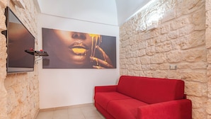 Un canapé rouge adossé à un mur en pierre à la texture marquée, un téléviseur fixé au mur et un grand tableau abstrait.