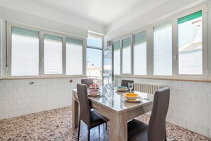 A dining area with a table set for four, white tiled walls, and large windows with blinds. - Casa Del Sol Alberobello (Alberobello)