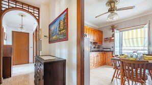 A spacious kitchen with wooden cabinets, a dining area with a wooden table and chairs, and a large window with striped curtains. - Casa Nonna Caterina Monopoli (Monopoli)