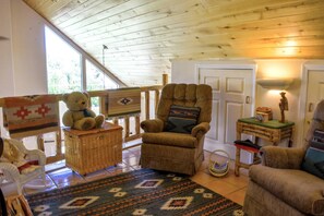 A cozy room with a wooden ceiling, a brown armchair, a wicker chair, a small table with a statue, and a patterned rug. - Creekside Cabin: Pet Friendly, Hot tub, Sled Hill, Walk to Shops, Dining & Springs, 2 Living Spaces (Pagosa Springs)