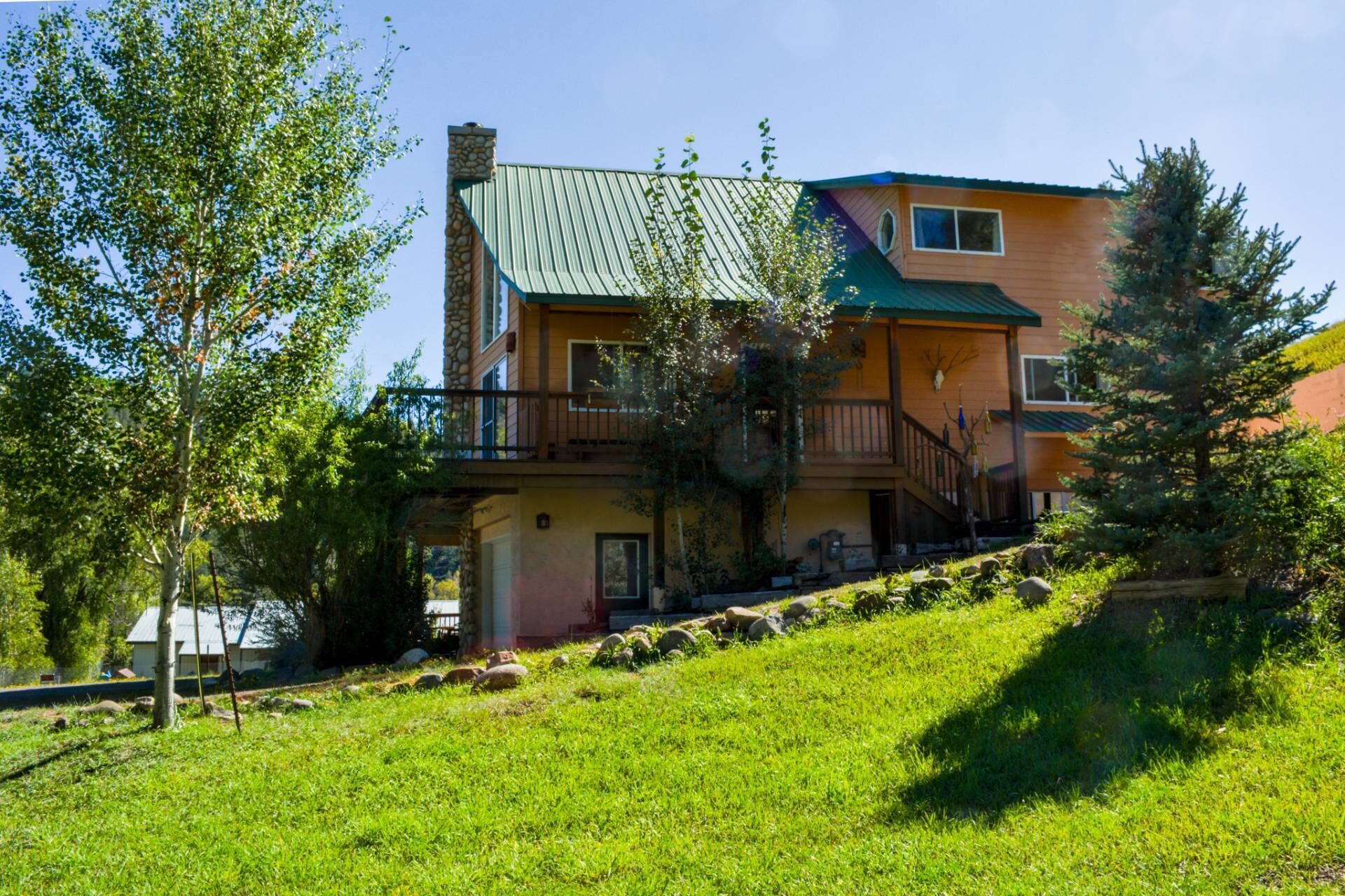 A two-story house with a green roof, a balcony, and a stone chimney.