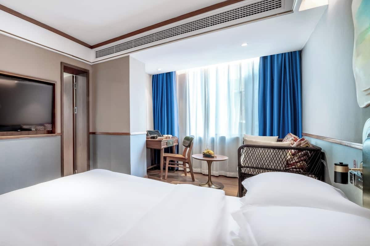 Une chambre d’hôtel avec un lit, un bureau et une chaise, une télévision et une fenêtre avec des rideaux.