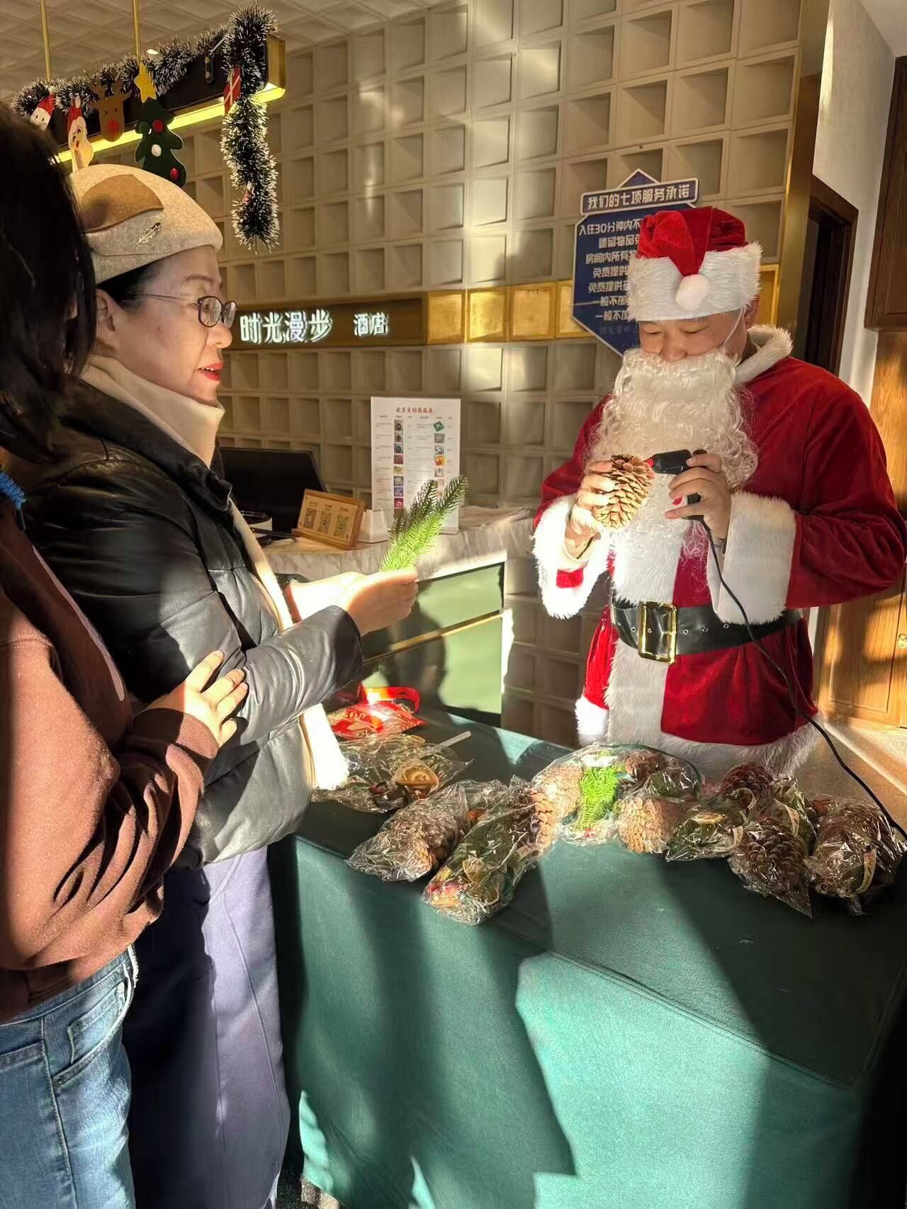 A person in a Santa costume holding a gift wrapped in a pine cone at a table with wrapped food items.