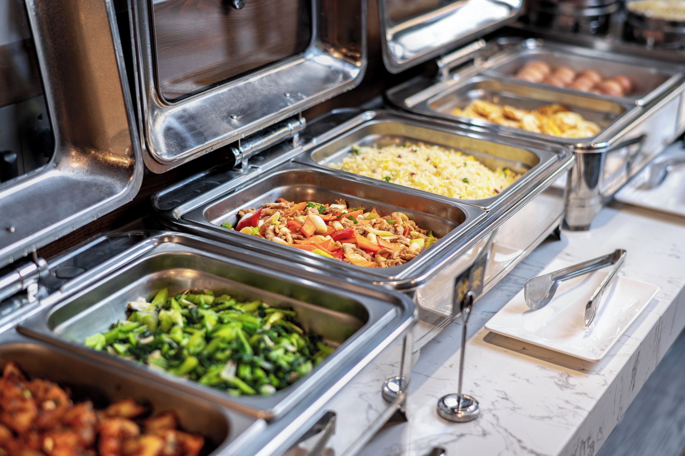 A buffet with multiple food stations including vegetables, rice, and meat dishes.