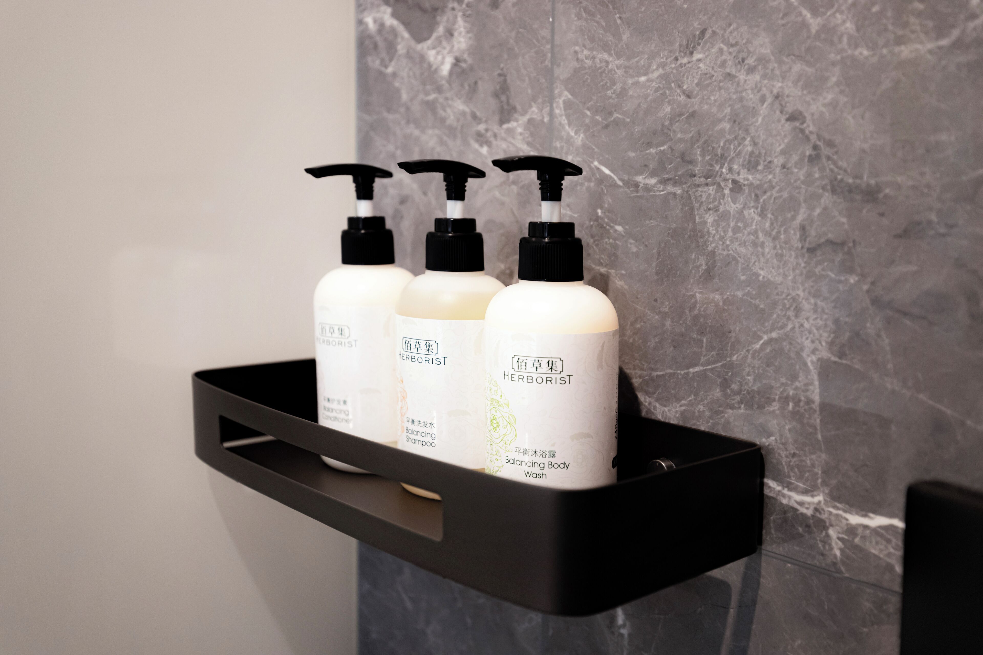 A black shelf with three white bottles of 'Herborist' balancing body shampoo and wash.
