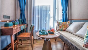 Une pièce avec un bureau en bois, une table ronde, un canapé et une fenêtre ornée de rideaux bleus.