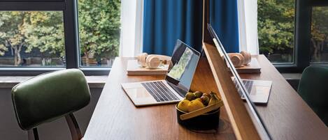 A modern office space with two laptops on a wooden table, a bowl of fruit, and a pair of headphones.