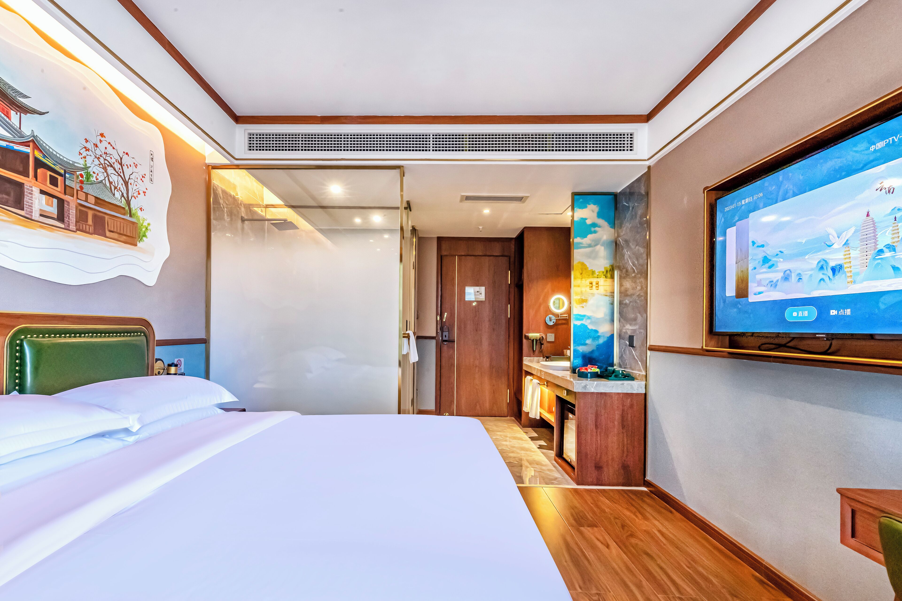 Une chambre d’hôtel avec un lit, un téléviseur fixé au mur, un bureau en bois et une salle de bain visible à travers une porte ouverte.