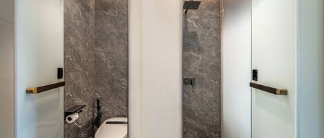 A modern bathroom with a toilet, a shower, and a glass partition.