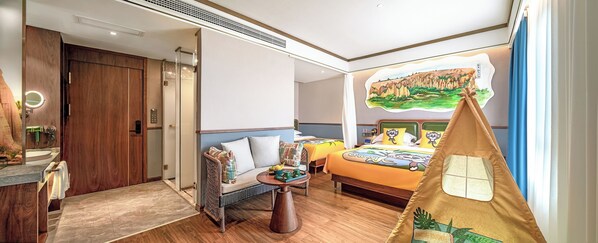 A hotel room with a wooden wardrobe, a round mirror, a bed with cartoon-themed bedding, a small table with fruits, and a tent-like decoration.