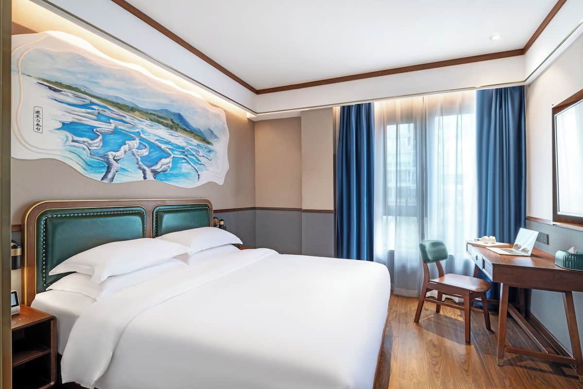 Une chambre d’hôtel avec un lit, un bureau, une chaise et une grande fenêtre avec des rideaux.